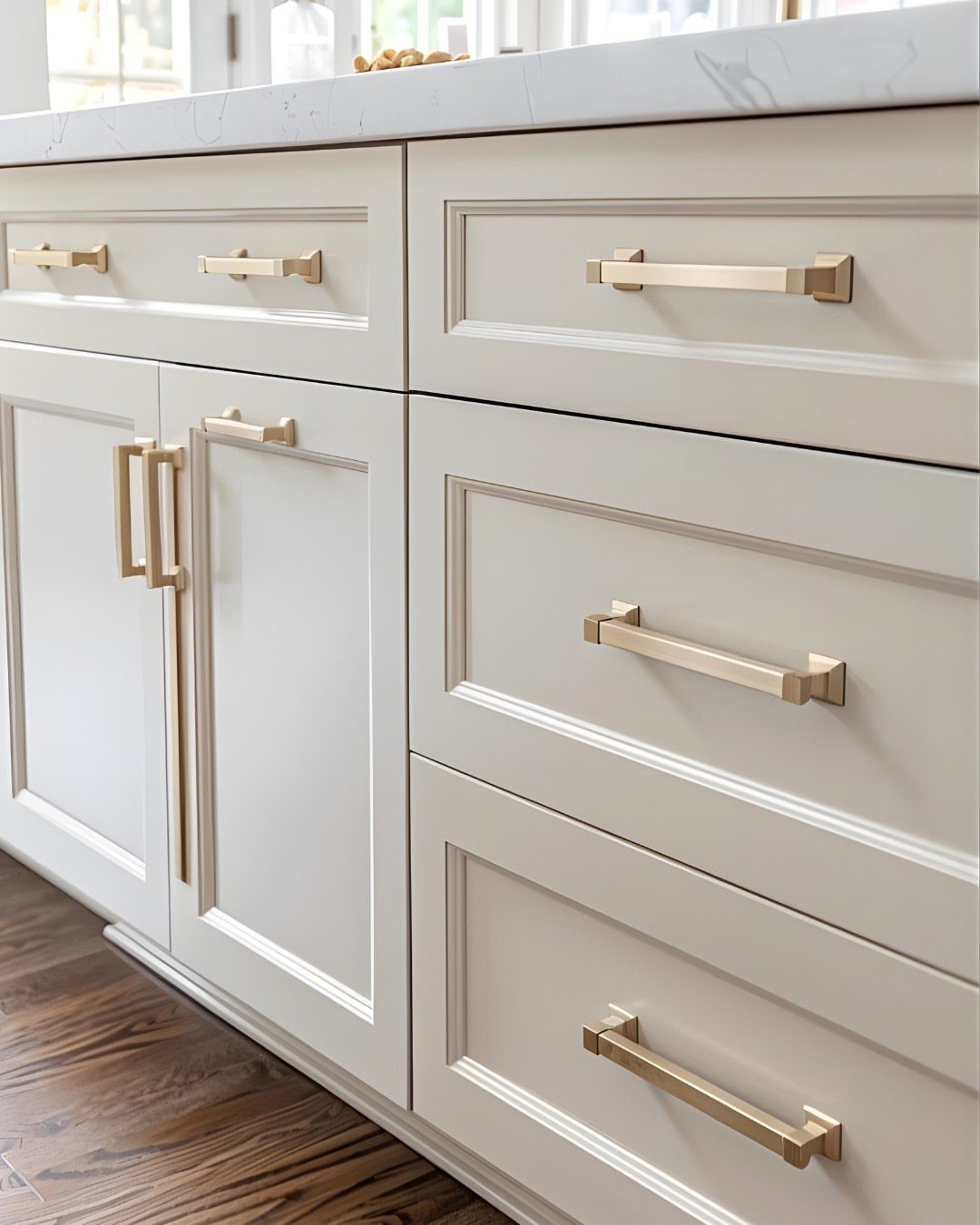 Off-white shaker kitchen cabinets with gold handles and dark wood flooring