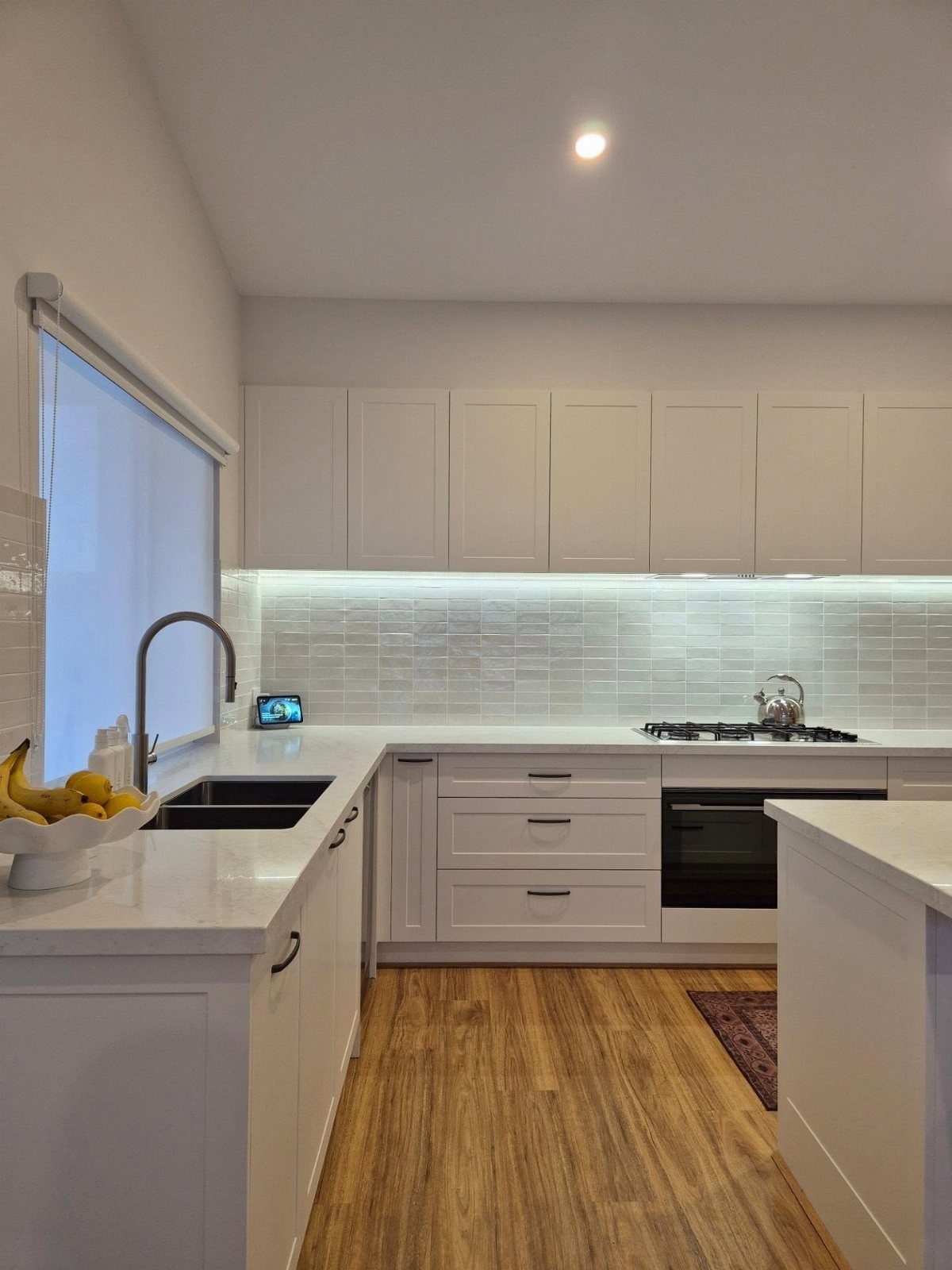 White quartz countertops in a bright kitchen with white cabinets and wooden floors.