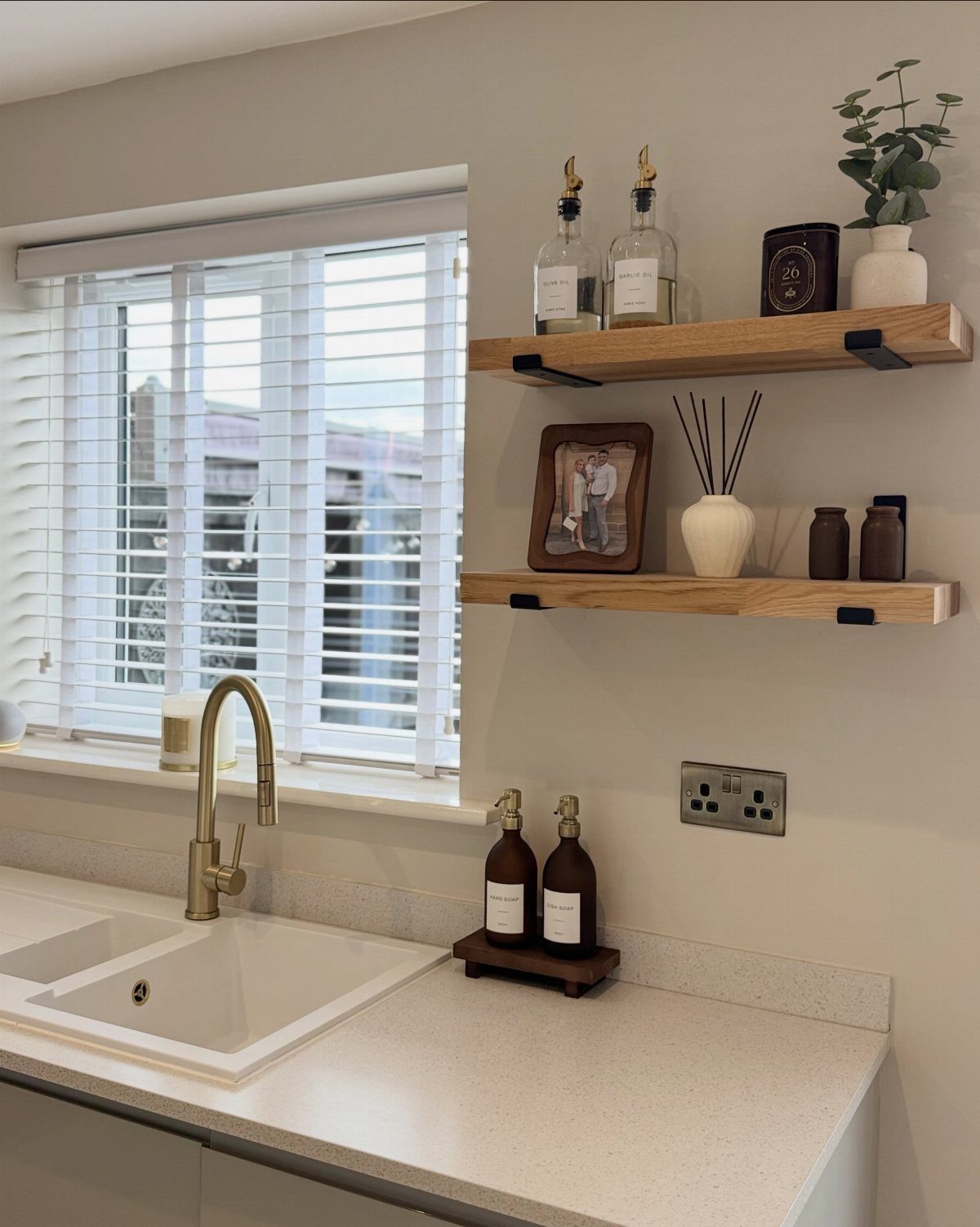White kitchen countertop and sink with light wooden floating shelves on beige wall