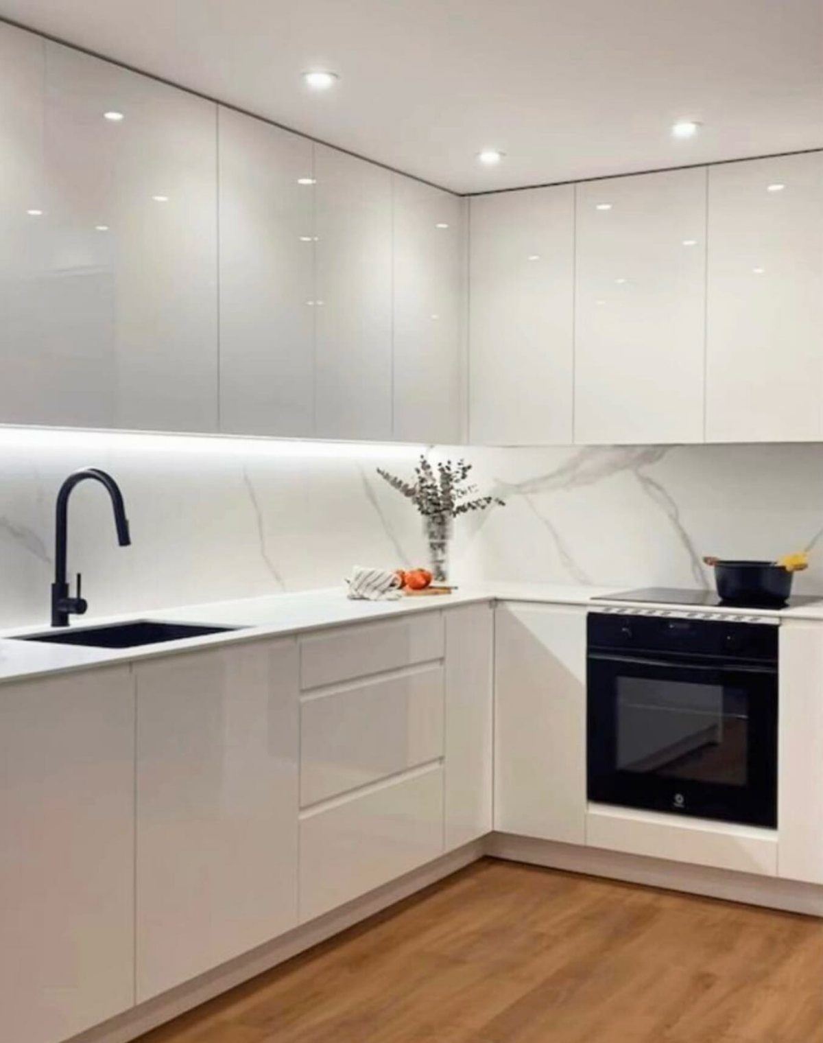 Modern white kitchen featuring a black built-in oven and black faucet fixtures.