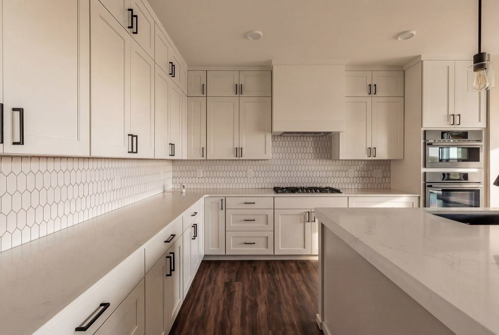 White kitchen cabinets with black hardware, white countertops, and dark wood floors.