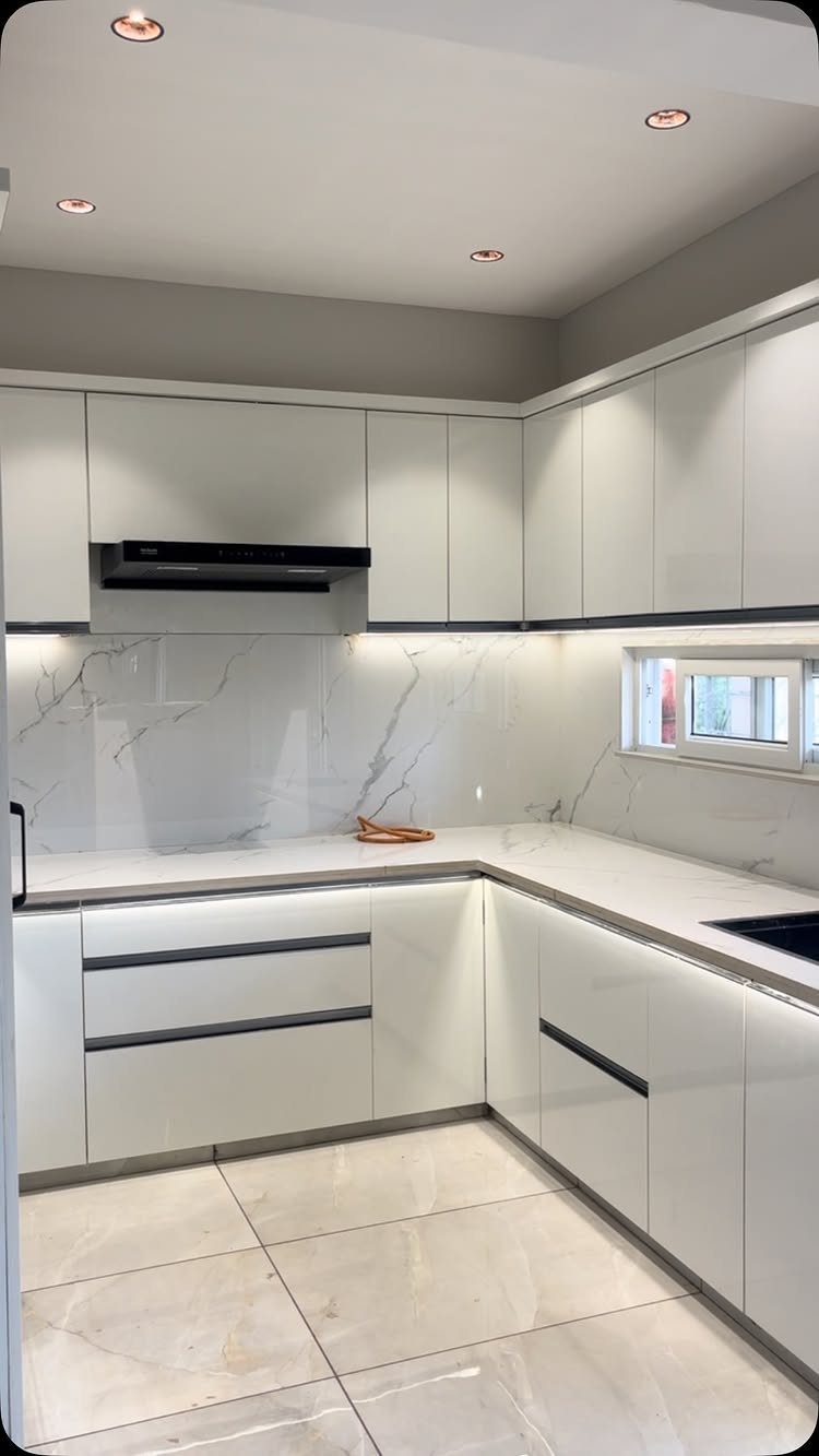 White glossy kitchen cabinets with black hardware and white marble countertops.