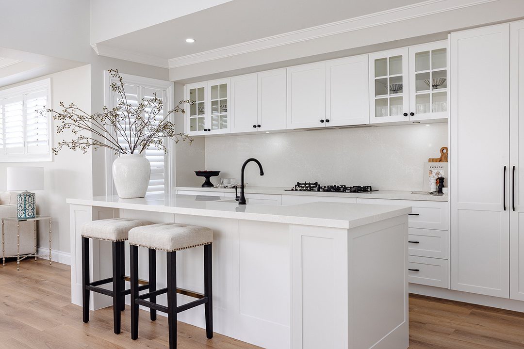 White kitchen with white cabinets, black hardware, and white bar stools with black legs.