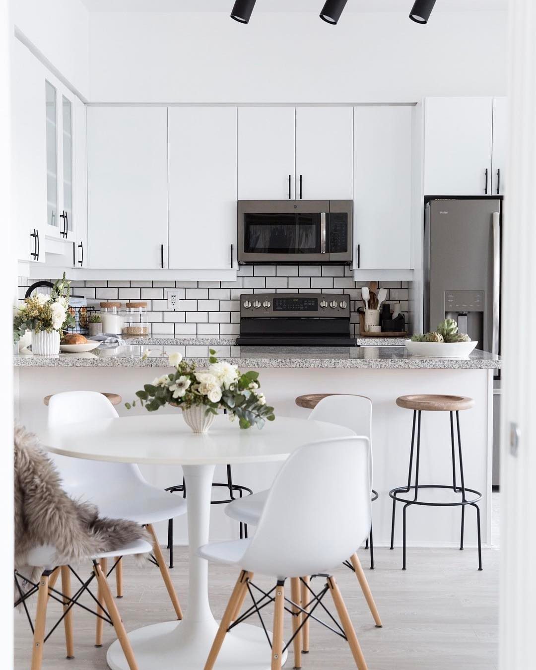White subway tile backsplash in a bright kitchen with white cabinets and black hardware