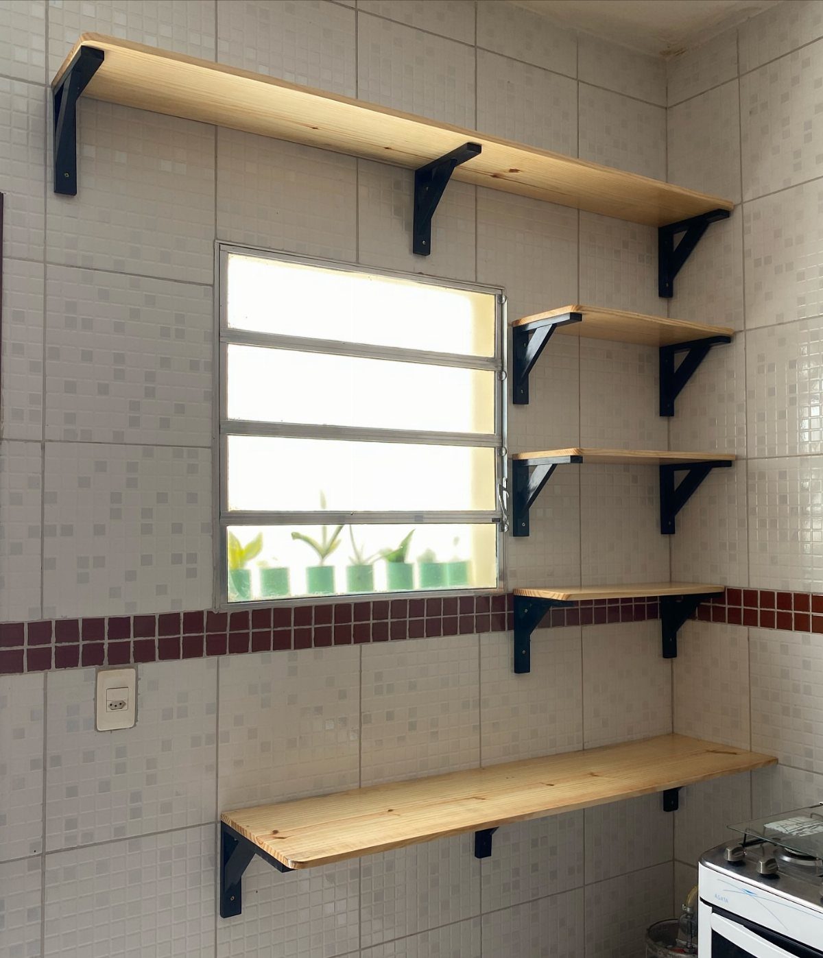 Wooden shelves with black metal brackets mounted on a white tiled kitchen wall.