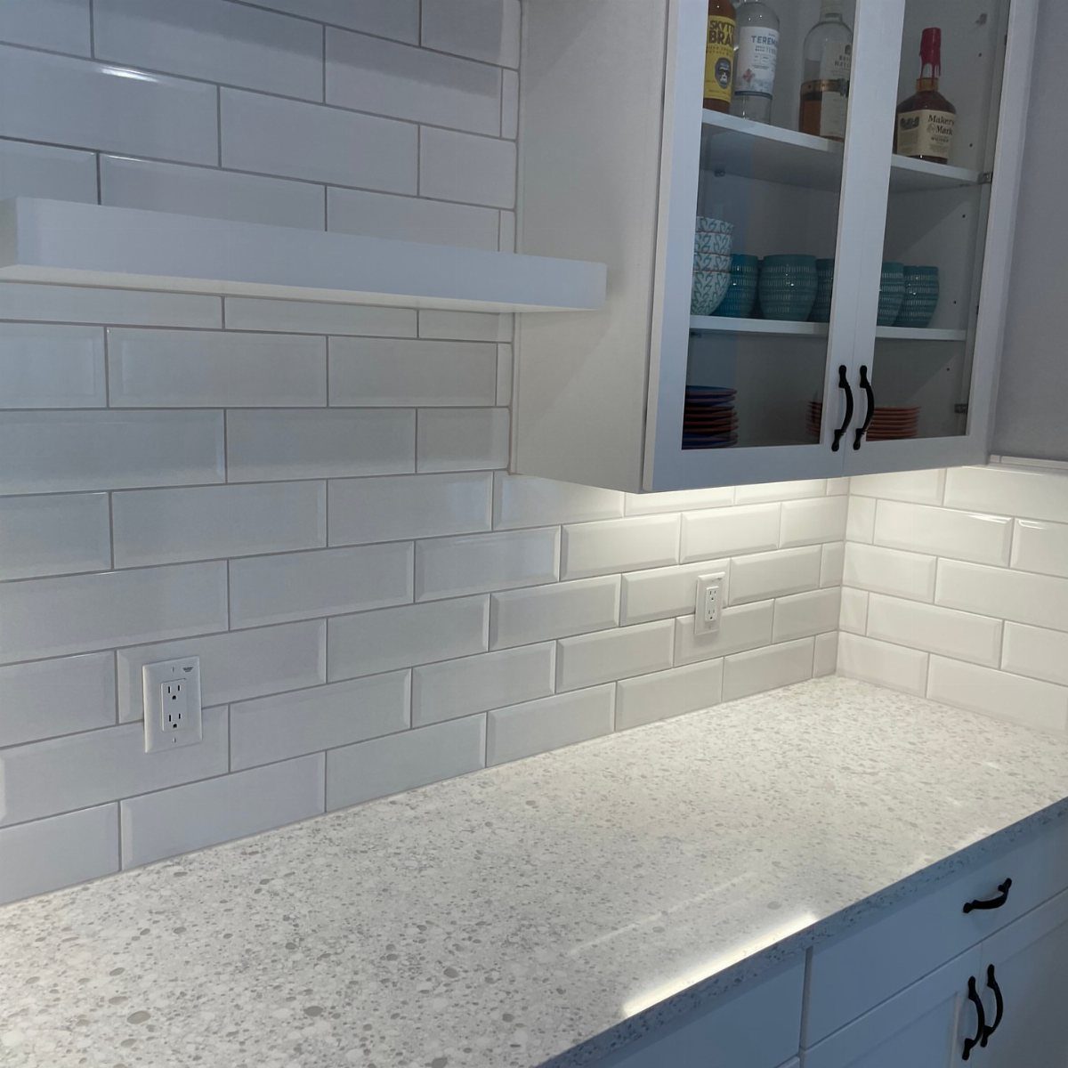 Glossy white subway tile backsplash with white quartz countertops and white cabinetry.