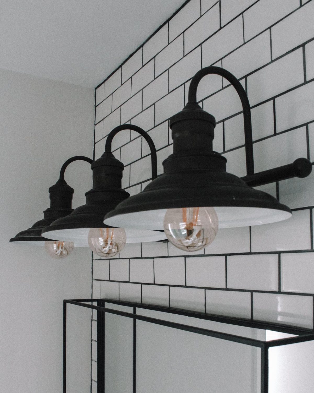 Black industrial wall lamps mounted on white subway tile with dark grout lines.