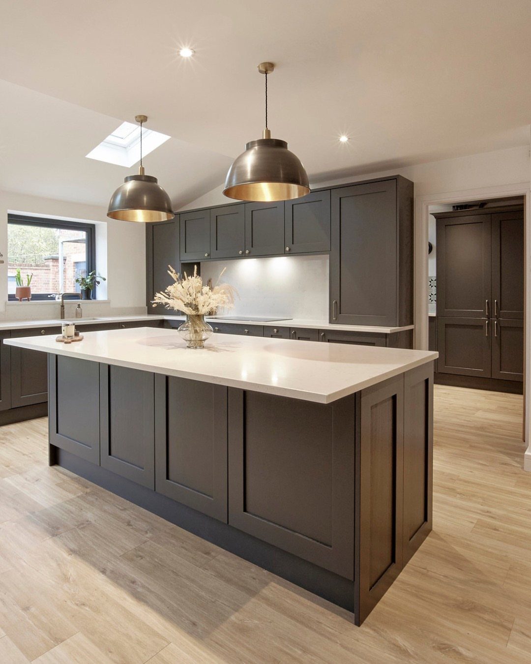 Dark gray kitchen cabinets and island paired with light brown wood flooring.