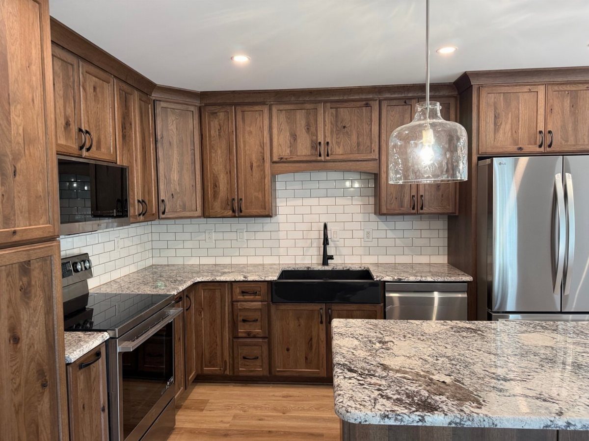 Wood cabinets and wood floors in a kitchen with granite countertops and stainless appliances.