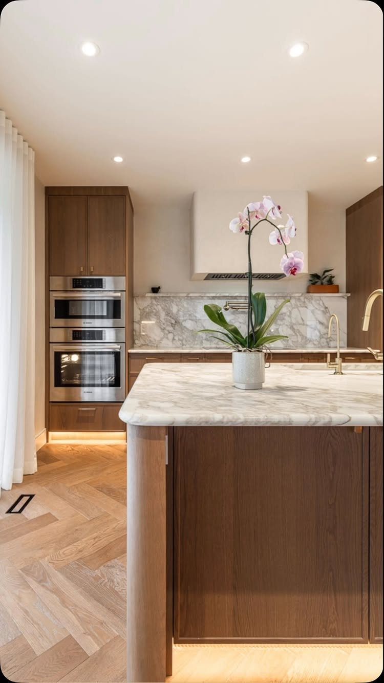 Brown wood kitchen cabinets and island with light brown herringbone wood floors.